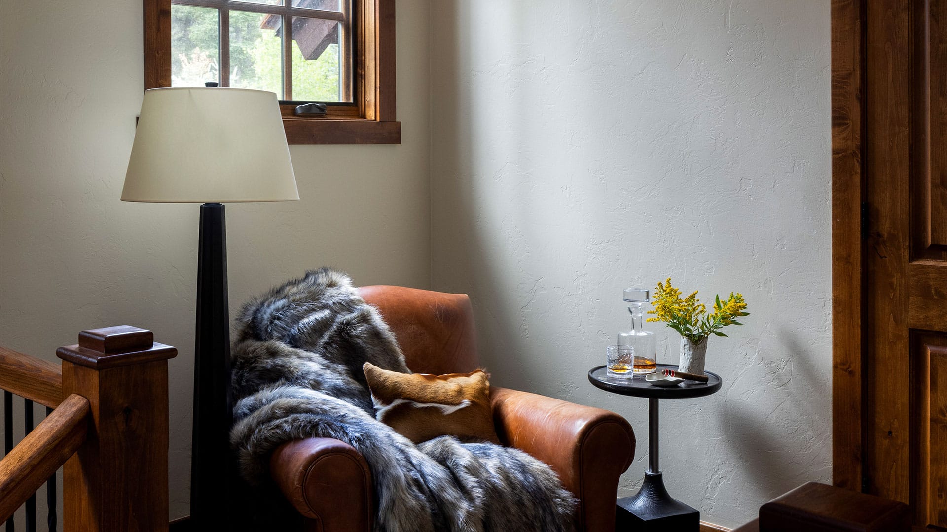 Nida Risto Interiors - Jackson Hole, Wyoming - Interior of a Snake River Sporting Club house showing a large leather armchair covered in a fury blanket set in a beam of light coming from a high window.